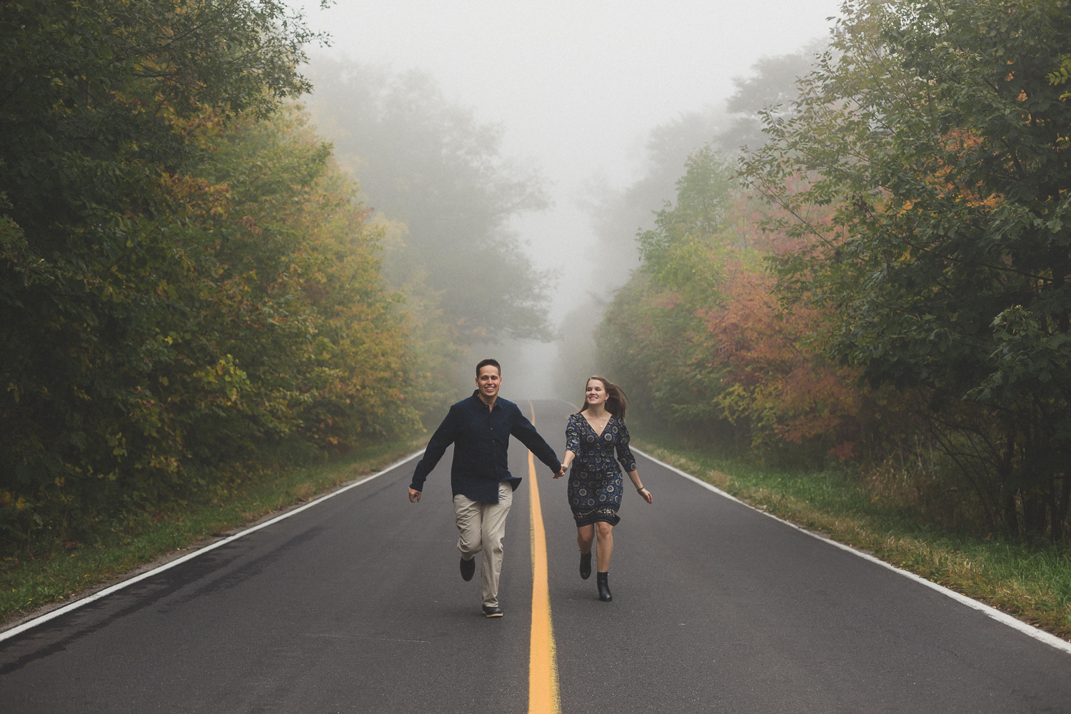 Couple running down foggy abandomed road in the fall