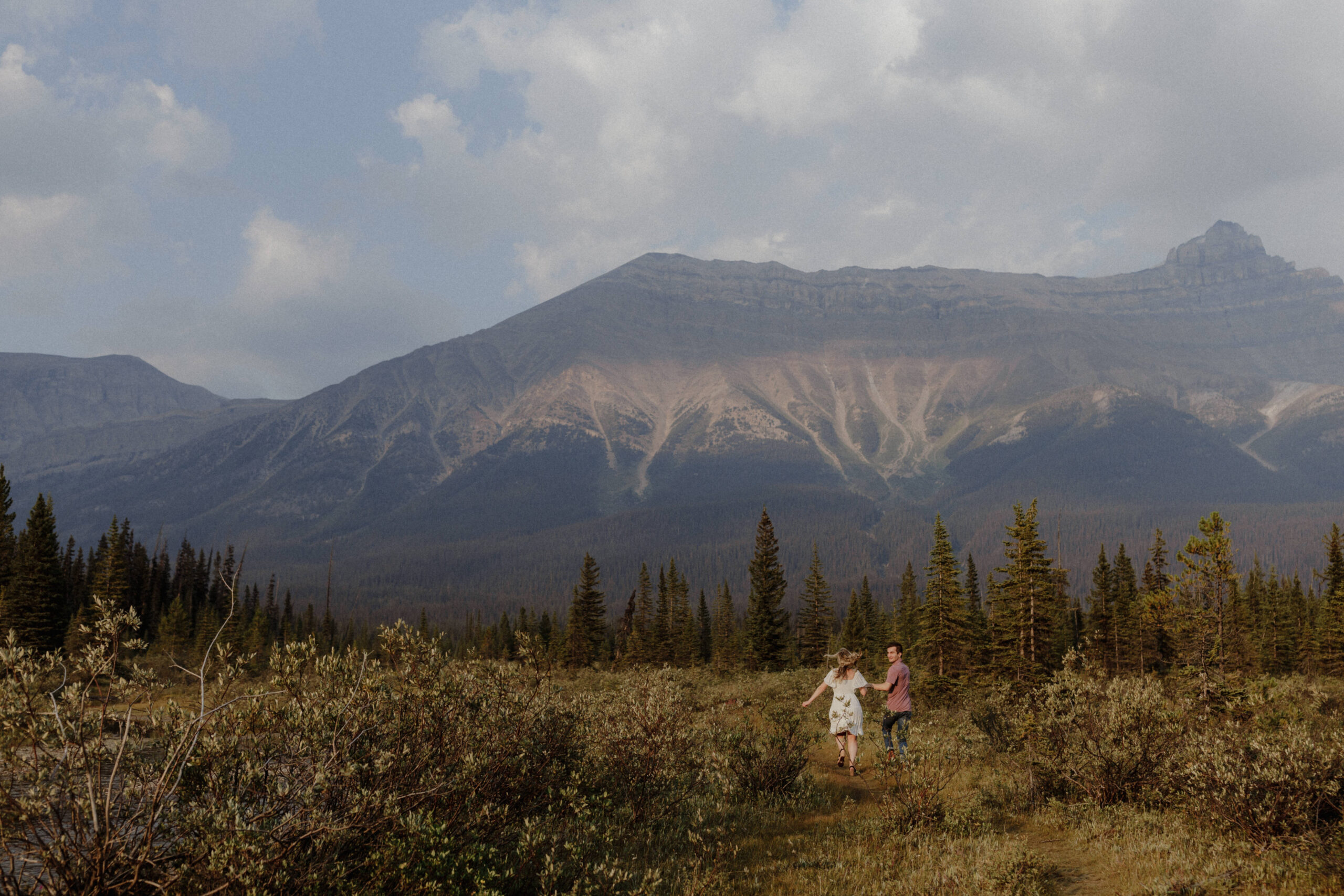 Two people walking through a field with mountains in the background in the rocky mountains in banff alberta.